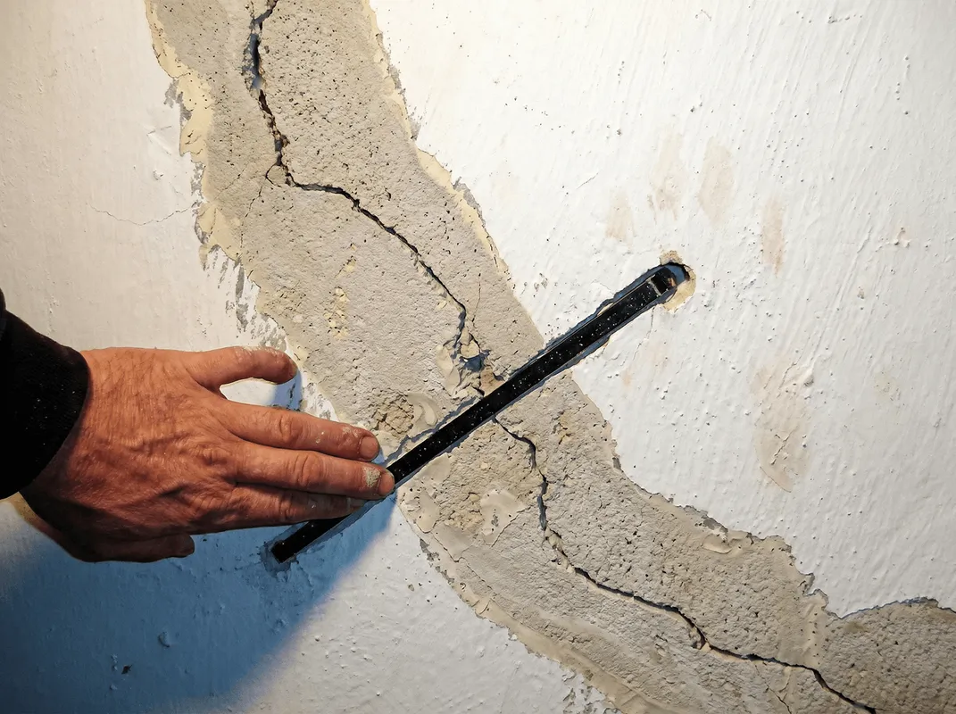 A wall with a large crack is being inspected by a professional in Ann Arbor, MI